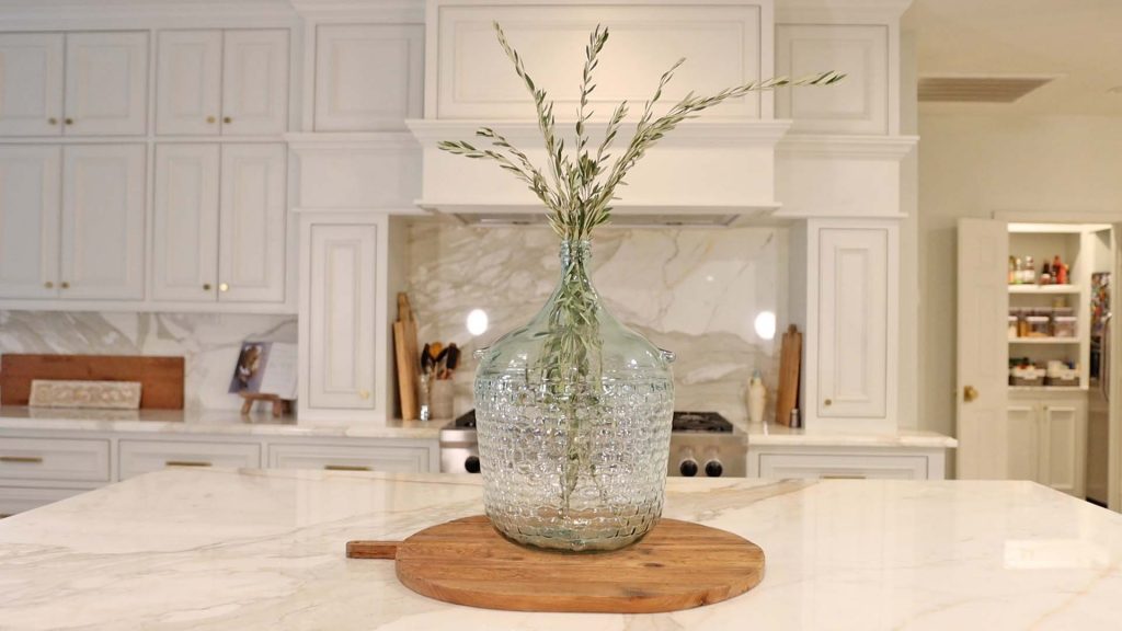 Amitha Verma adds olive branches to her large glass jar from Village Antiques and places it on top of her breadboard as a kitchen island centerpiece.