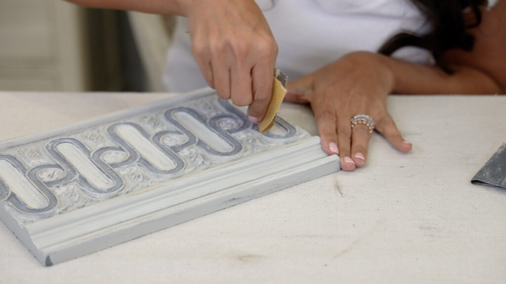 Once all paint layers are complete and dry on a furniture makeover, Amitha Verma distresses the piece with sandpaper.
